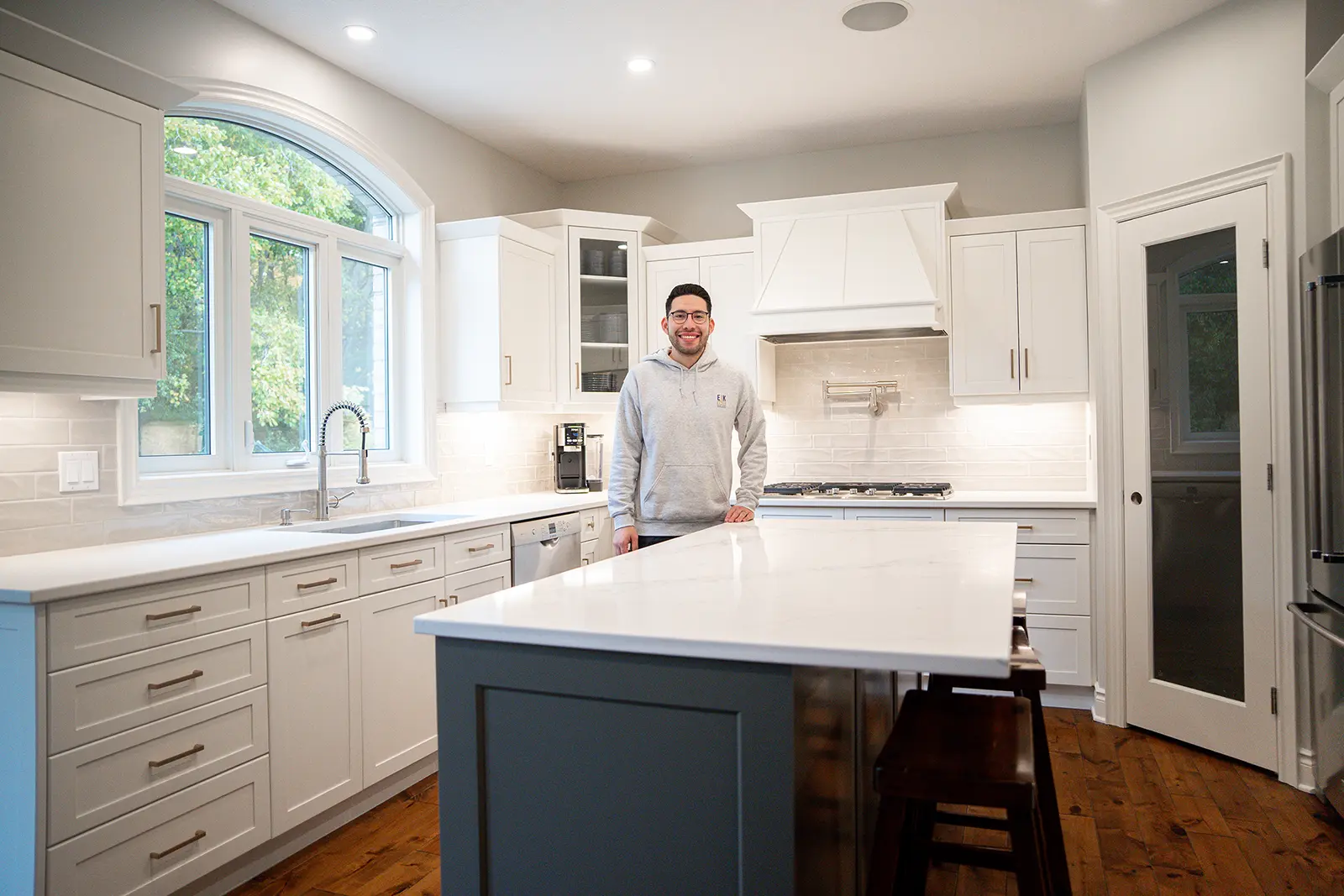 EKR_Steam-two-tone-kitchen-3_1600 Helaman Hernandez, owner of Elegant Kitchen Restoration, standing in a newly refinished white kitchen showcasing professional cabinet refinishing work